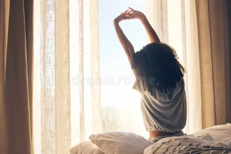 A black woman stretching in front of her window.